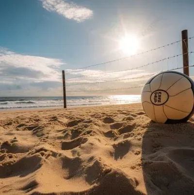 Vôlei de praia em uma faixa de areia com rede, ondas do mar e sol brilhante.