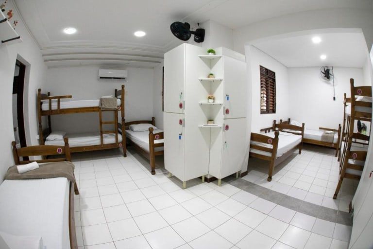 Quarto de dormitório claro e branco com beliches, camas de solteiro, escrivaninha, ar-condicionado e piso de azulejo.