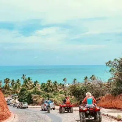 Quadriciclos descendo uma estrada costeira em direção a um oceano turquesa sob um céu azul.
