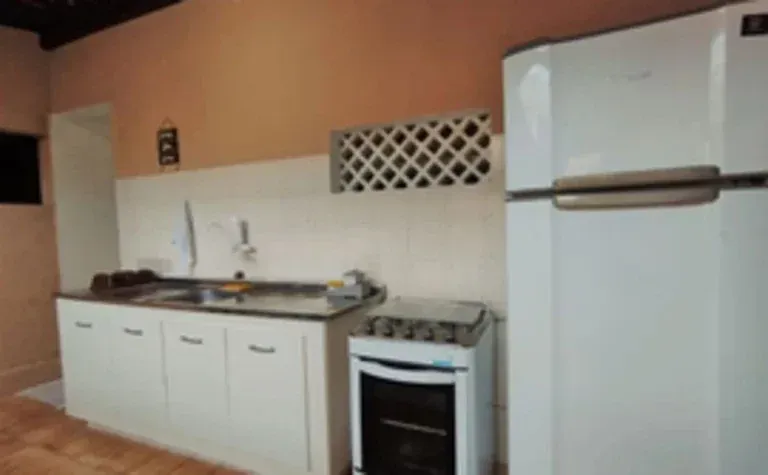 Cozinha pequena com armários brancos, fogão, pia e geladeira contra paredes cor de pêssego.