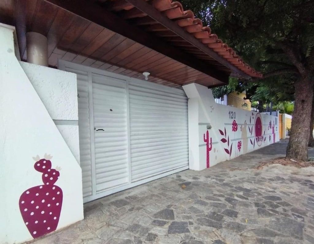 Porta de garagem branca ao lado de um caminho de pedra e parede pintada com desenhos de morangos cor-de-rosa sob uma árvore.