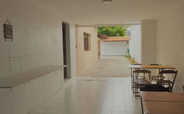 Pátio luminoso com piso de azulejo, mesa e cadeiras em uma passagem coberta, com acesso a uma garagem nos fundos.