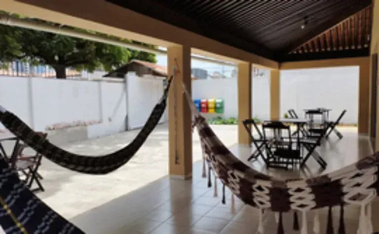 Varanda coberta com duas redes, uma mesa de jantar e cadeiras com vista para um pátio.