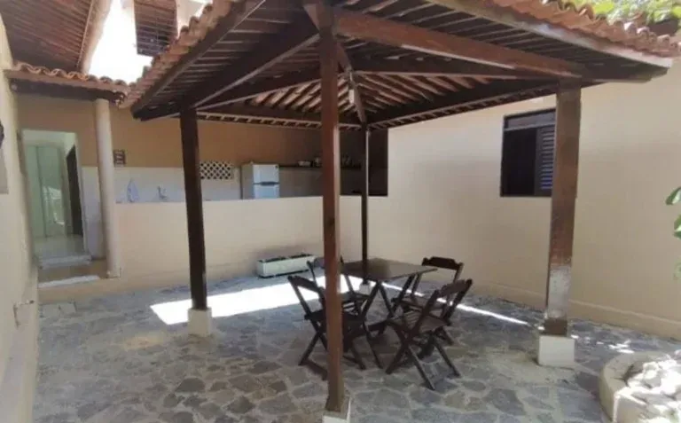 Pátio coberto de pedra com mesa e cadeiras de madeira sob um telhado de telhas em um pátio interno.