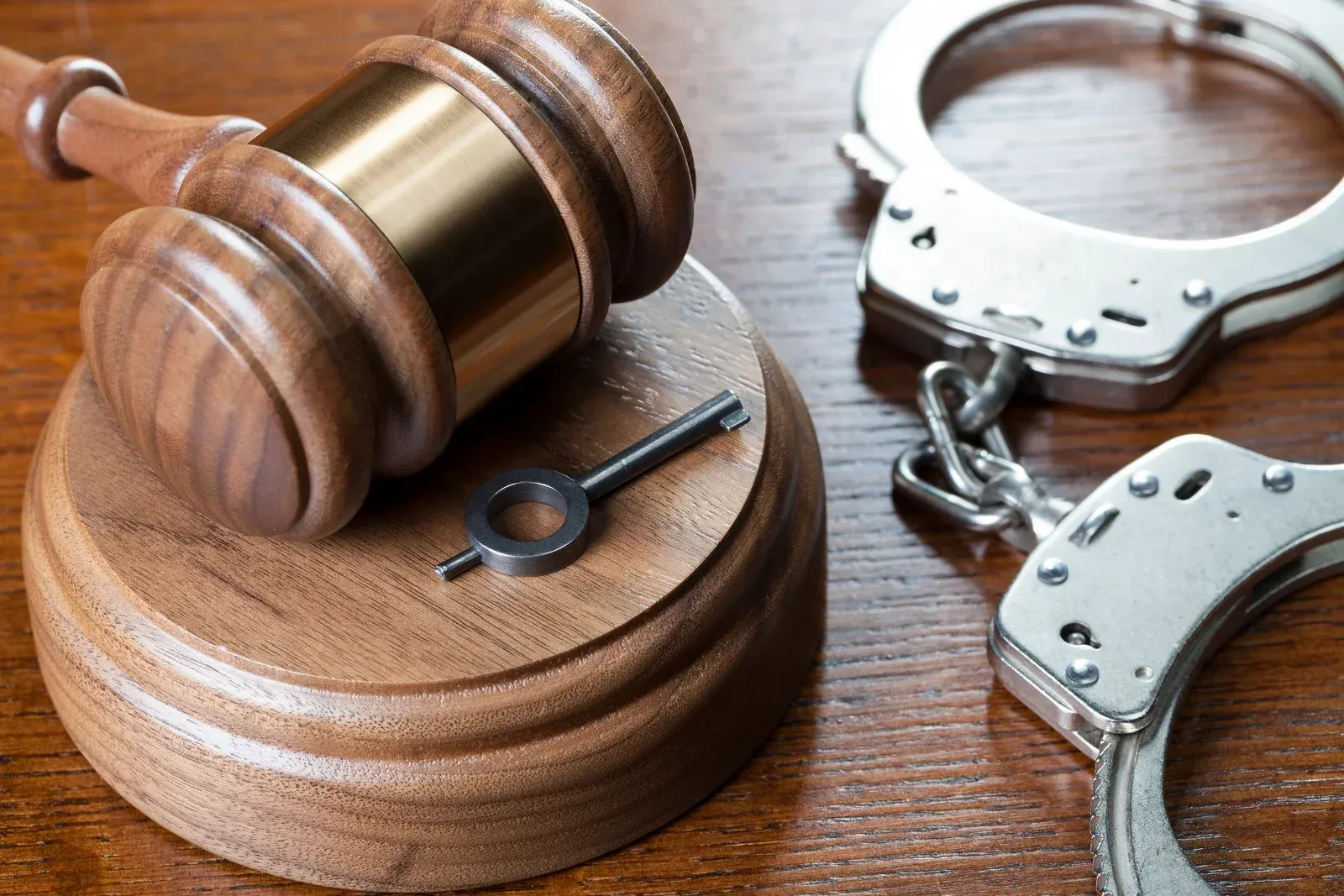 A wooden gavel with a key and handcuffs on a wooden table.
