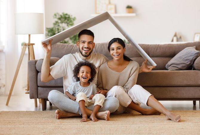 Family sitting on the floor in a cozy living room, smiling beneath a house-frame shape