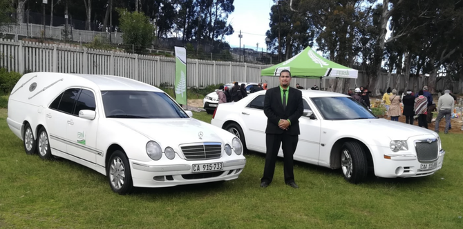 Two white limousines parked on grass with a person standing between them at an outdoor event