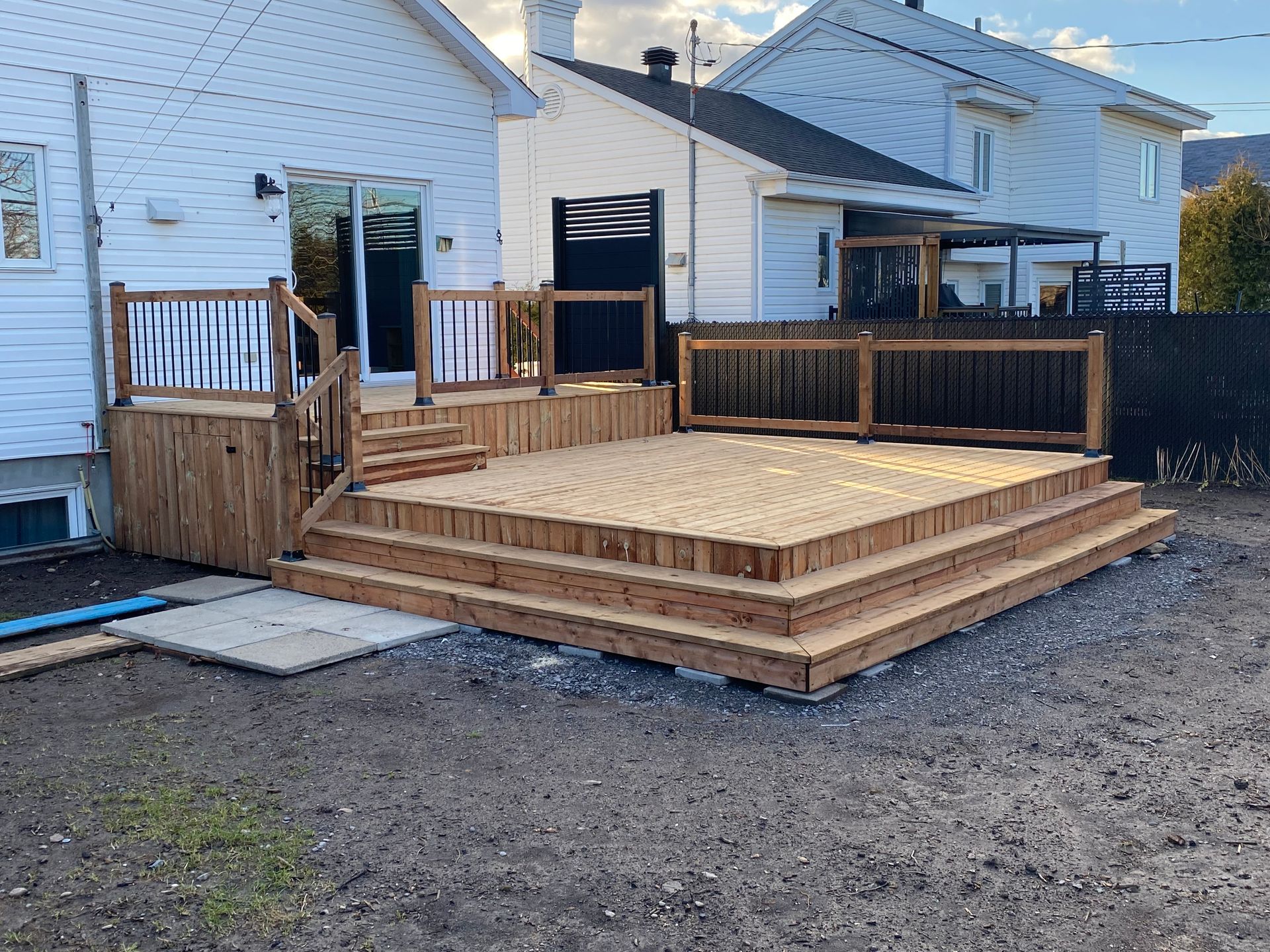 Une terrasse en bois avec des escaliers se trouve devant une maison blanche.