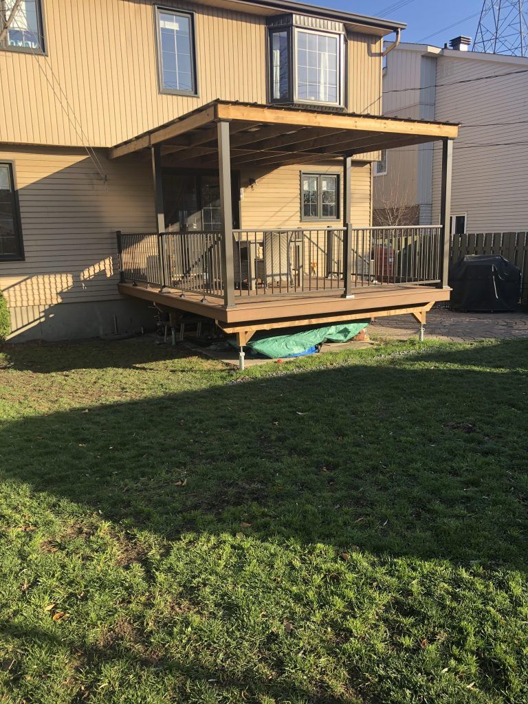 Une terrasse en bois se trouve sur une pelouse verte luxuriante devant une maison.