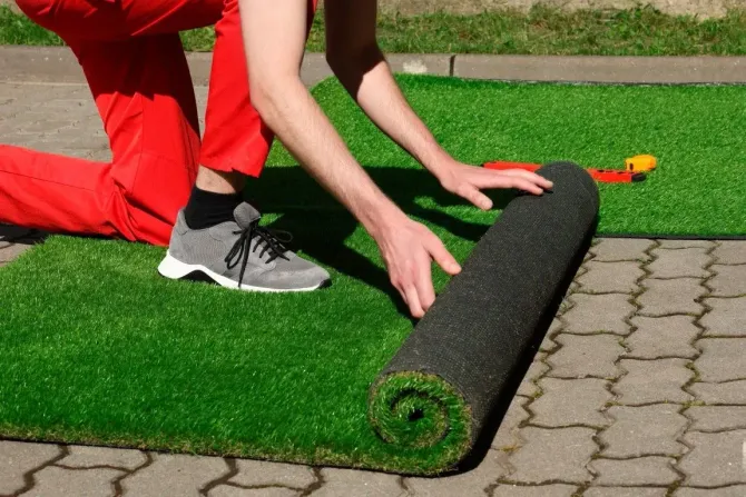 Person rolling out artificial grass on a stone patio.