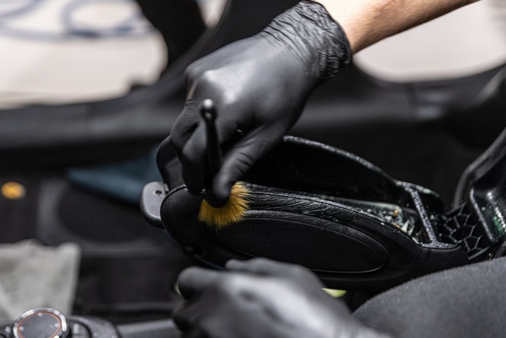 A Person Wearing Black Gloves Is Cleaning A Car Seat With A Brush — JA Toft & Co In Bundaberg Central, QLD
