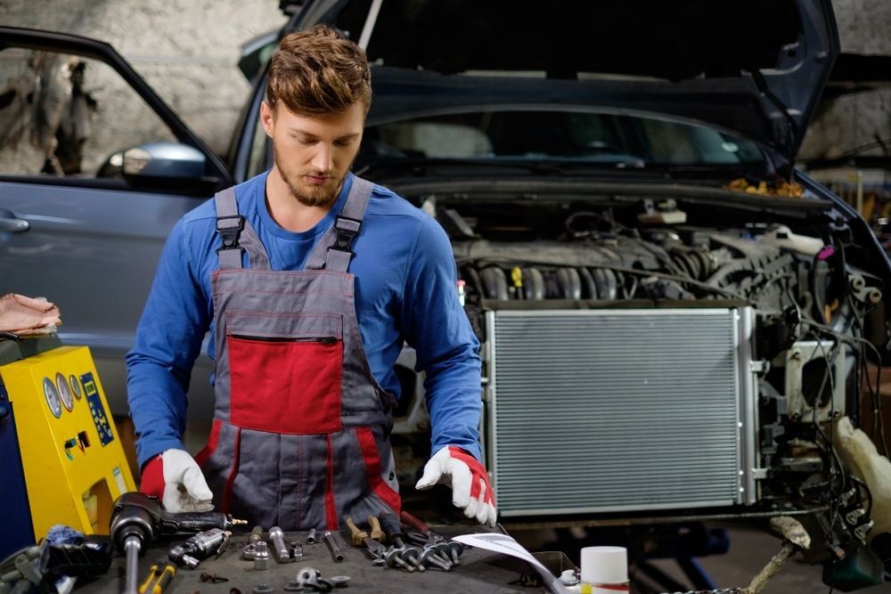 A Man Is Working On The Radiator Of A Car In A Garage — JA Toft & Co In Bundaberg Central, QLD