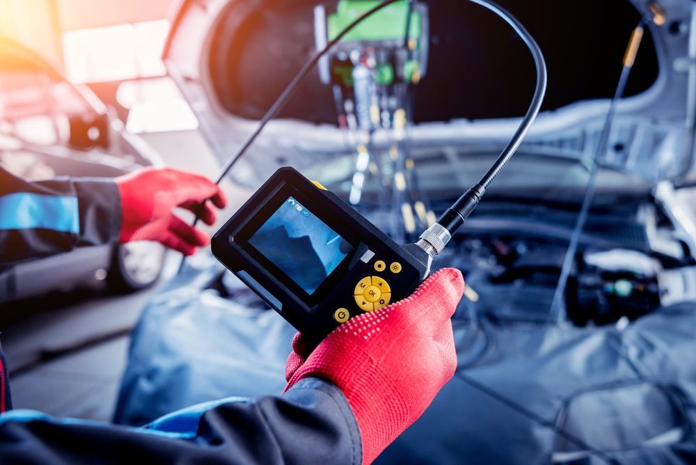A Mechanic Is Holding a Hose and A Camera in Front of A Car — JA Toft & Co In Bundaberg Central, QLD