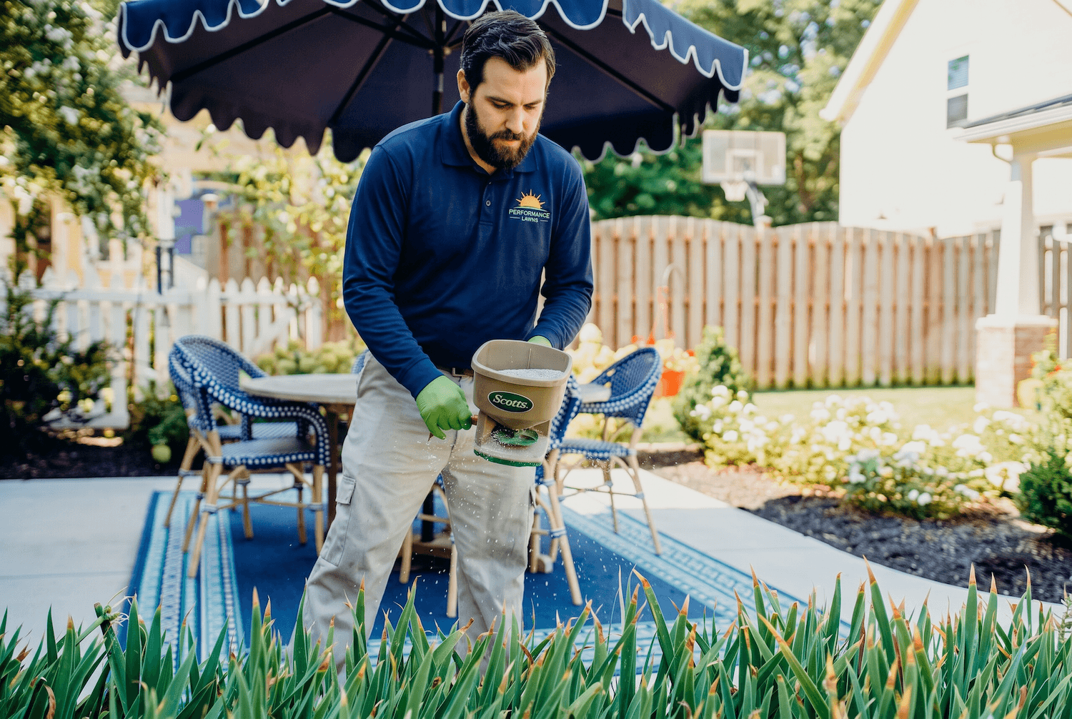 Person in blue overalls spraying a garden with a pesticide.