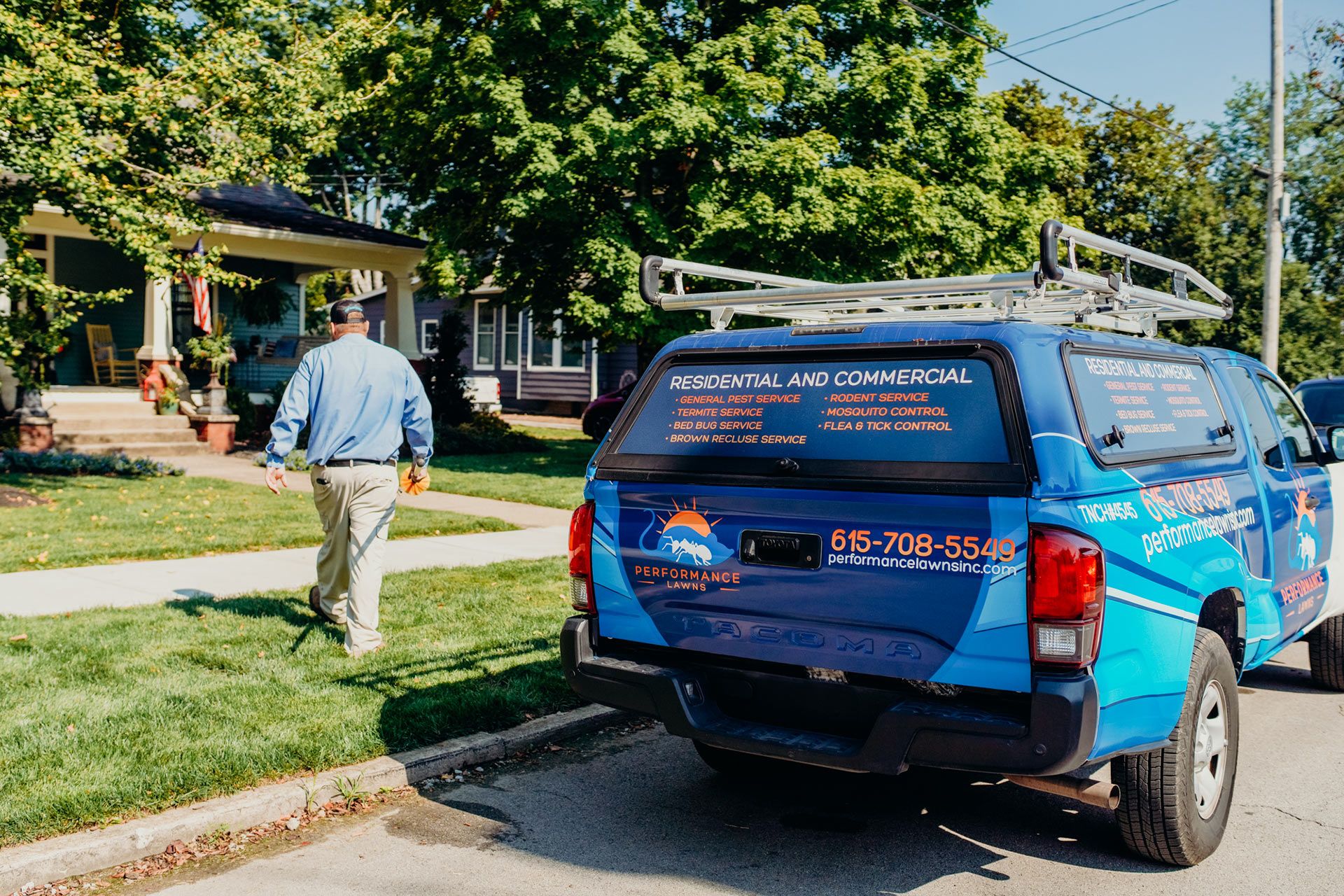 Blue service truck parked on a street with a man walking towards a house on a sunny day.