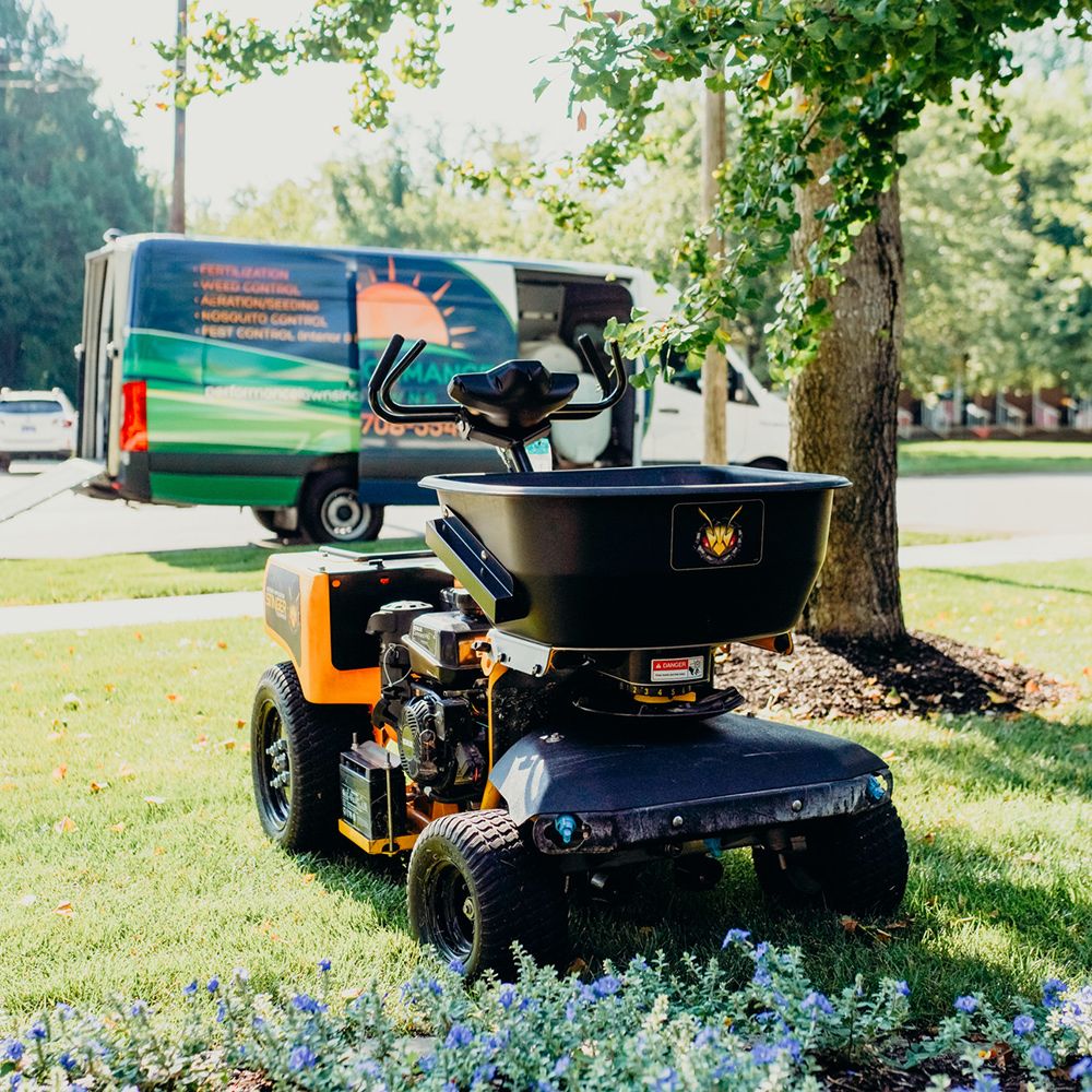Lawn spreader on grass with a branded van in the background.