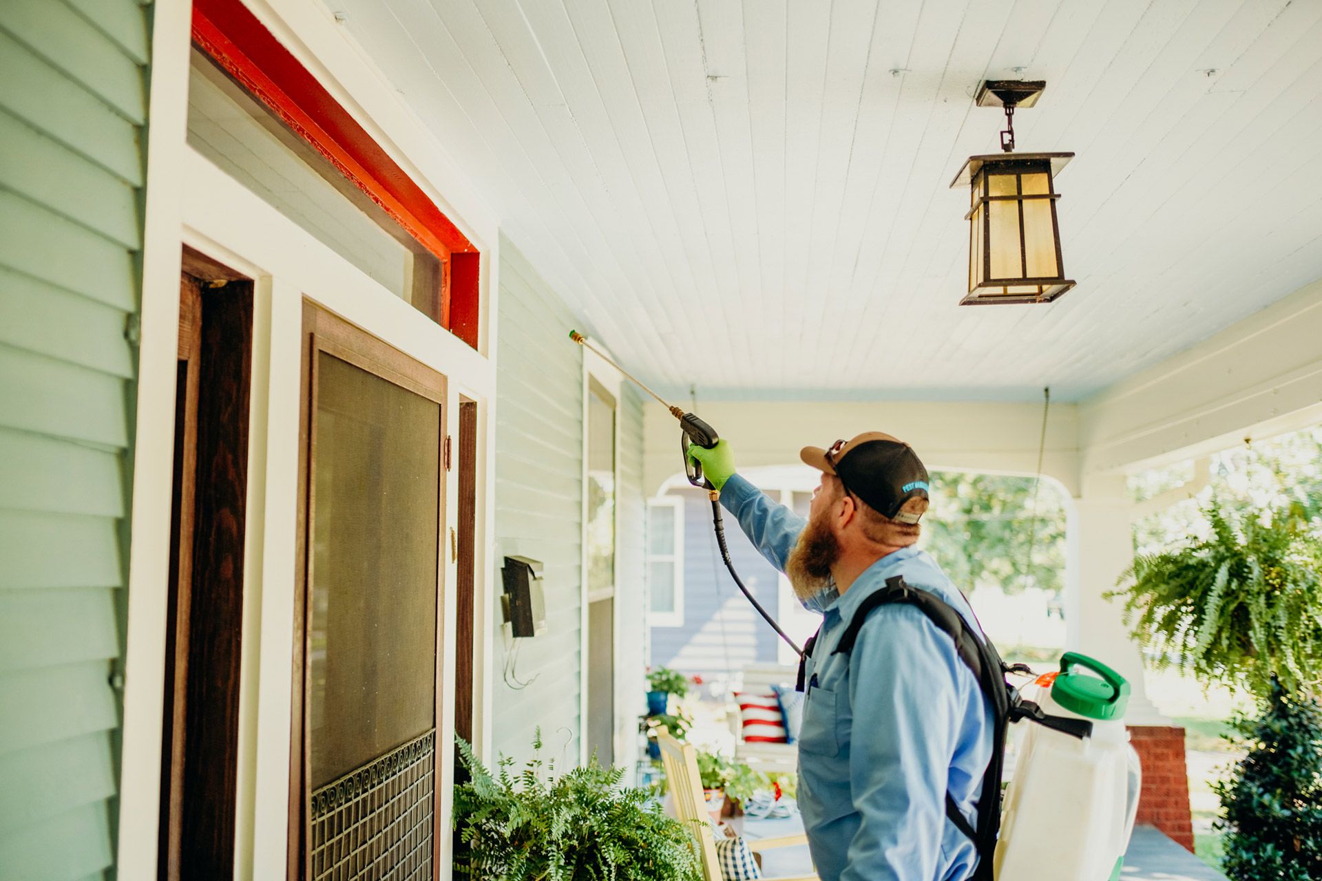 Pest control technician spraying a house exterior; blue and white paint, beard, spraying tool.