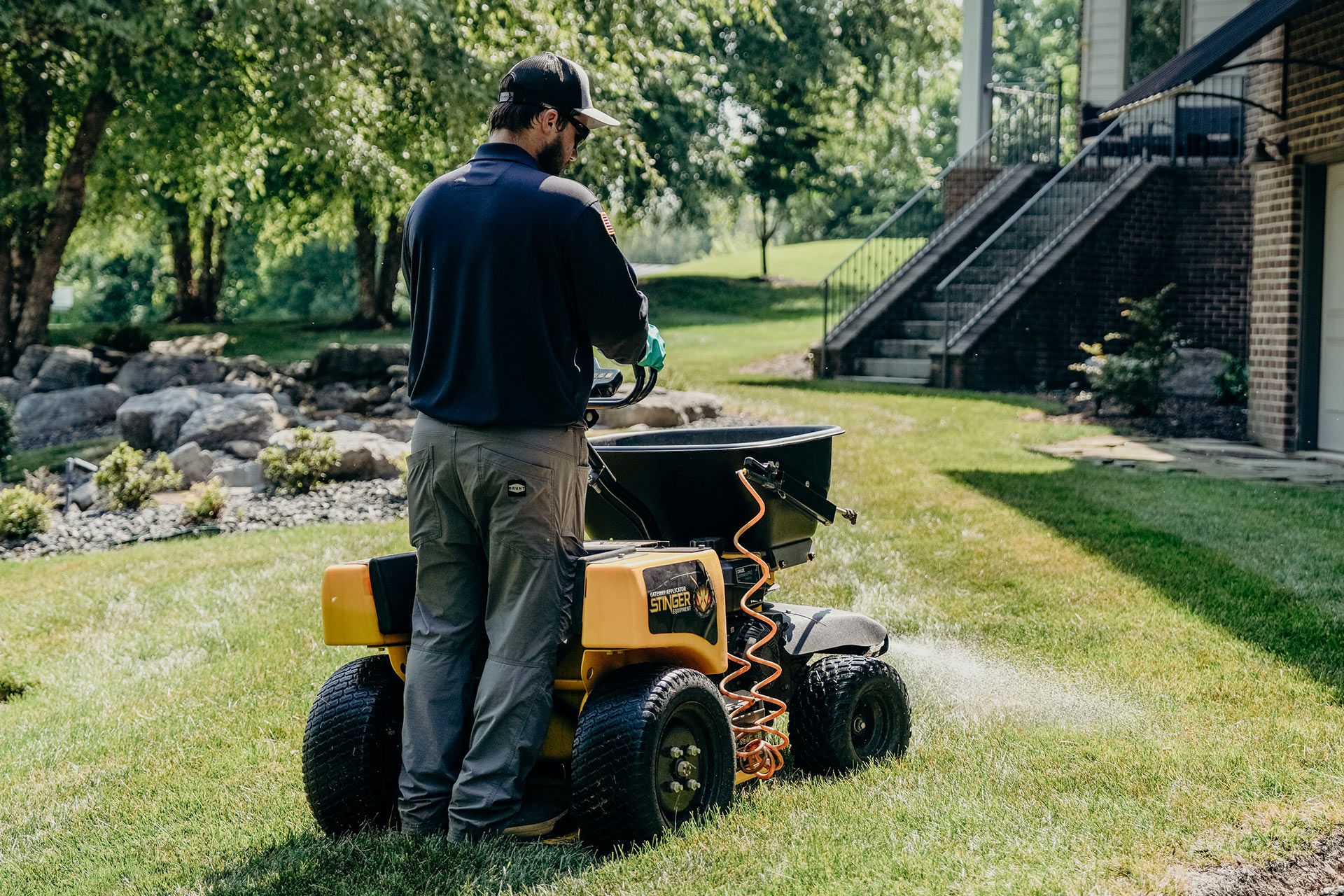 Man spreading fertilizer on lawn with a yellow and black machine.