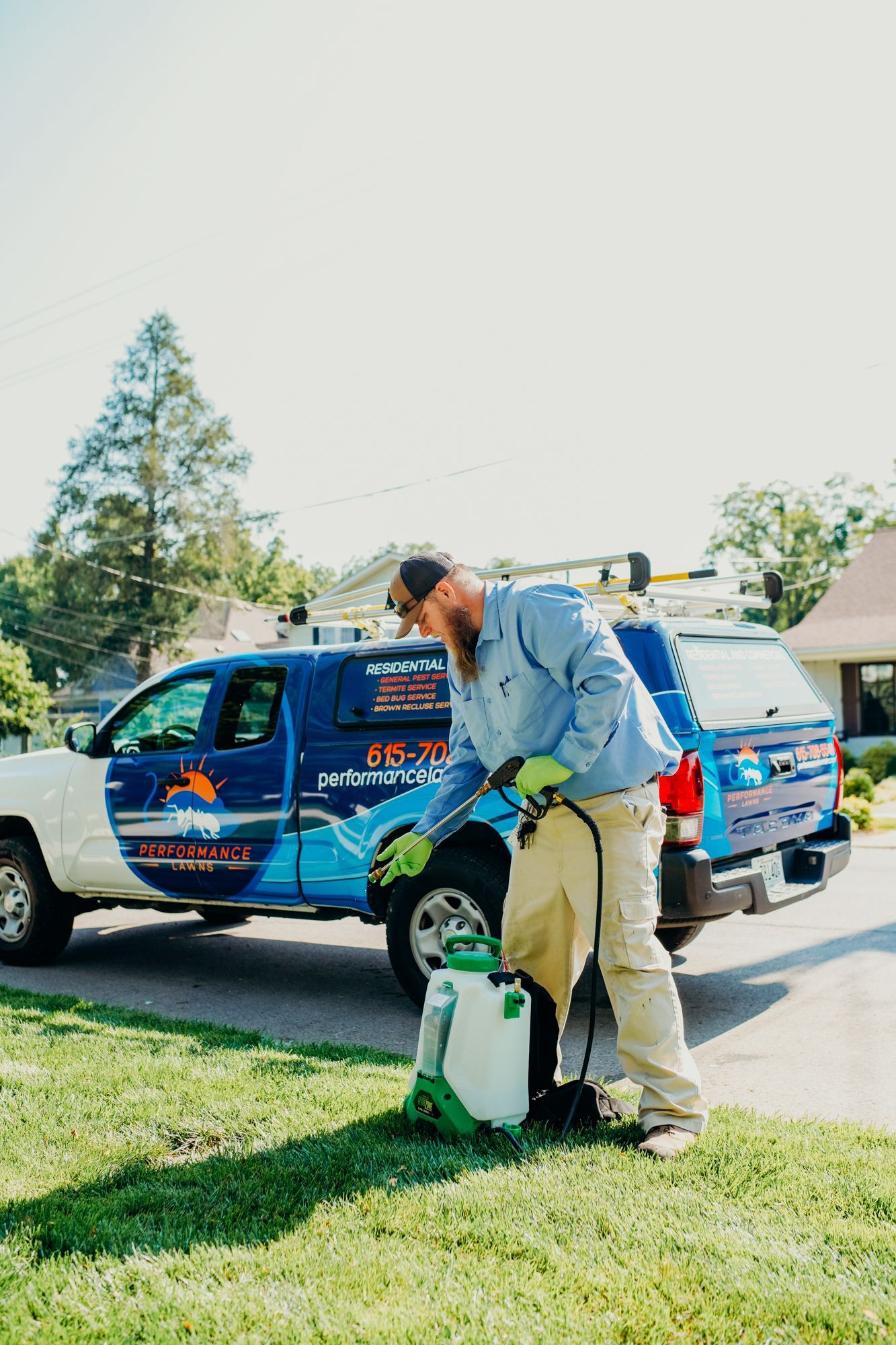 Pest control worker sprays grass. He stands next to a truck with a company logo on a sunny day.