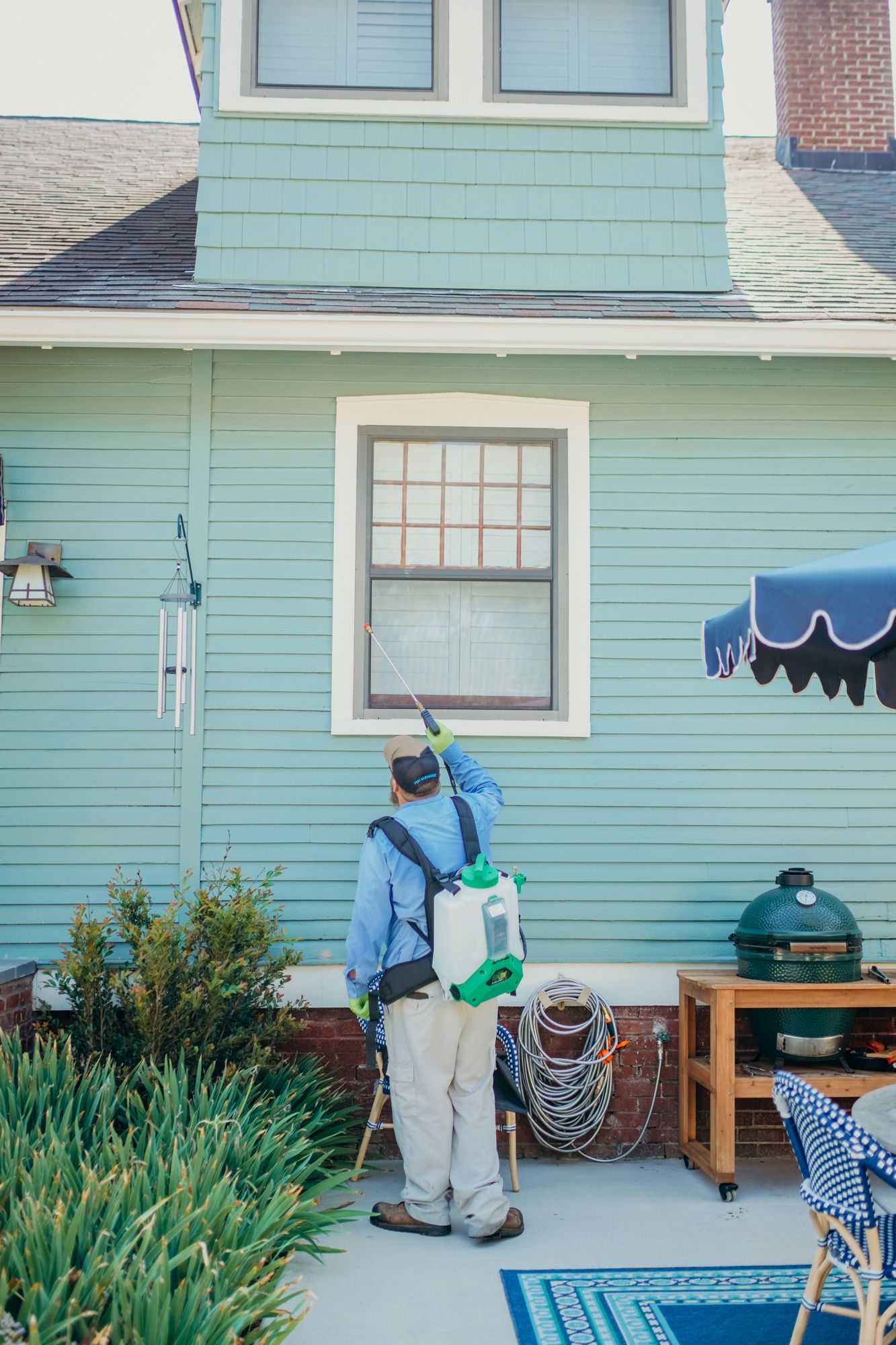 Pest control worker spraying insecticide on the side of a blue house.