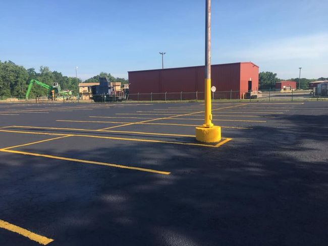 Newly paved parking lot with yellow painted lines and a red brick building in the background.