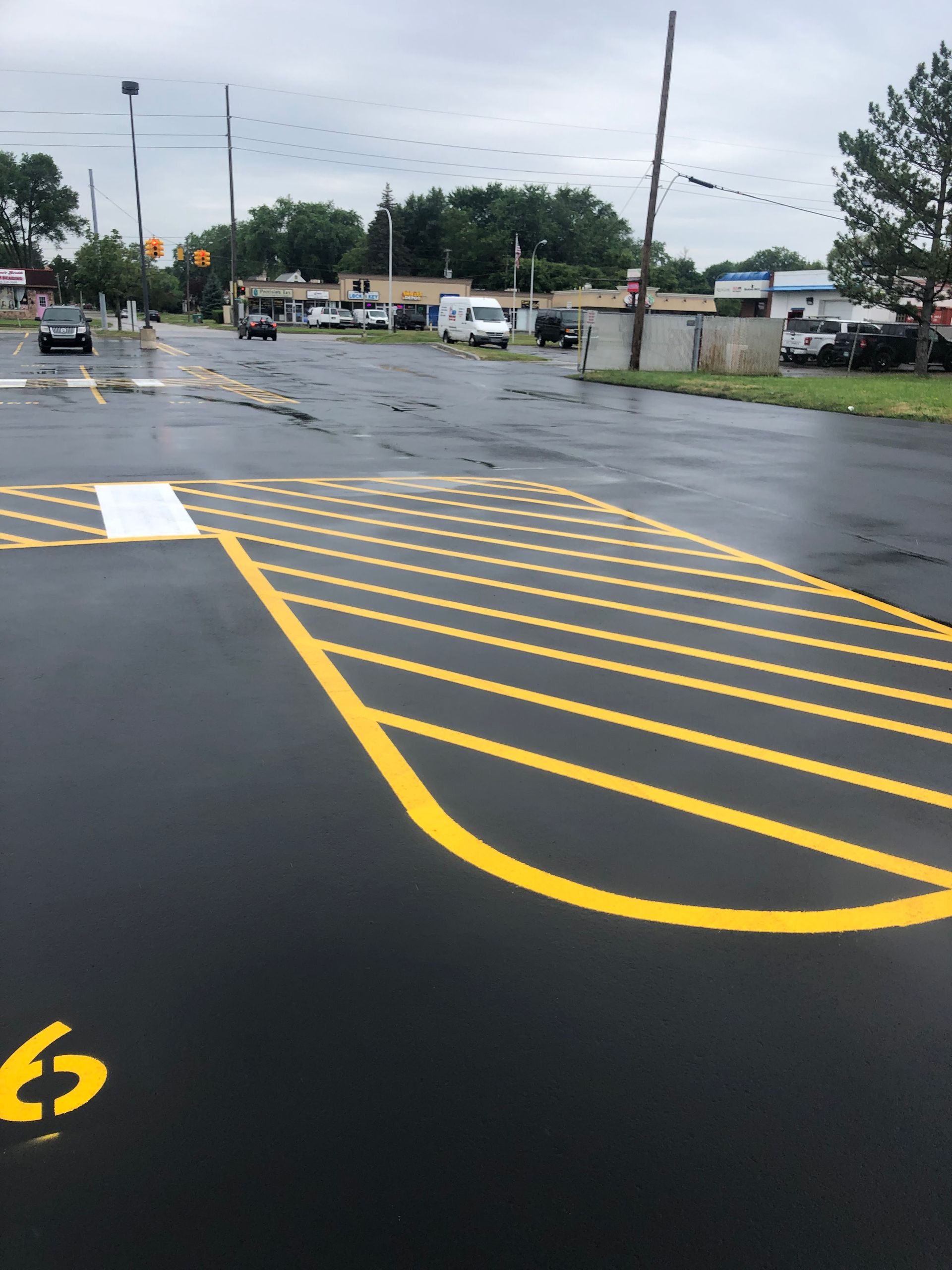 Yellow crosswalk markings on asphalt road. Buildings and parked vehicles in background. Overcast sky.