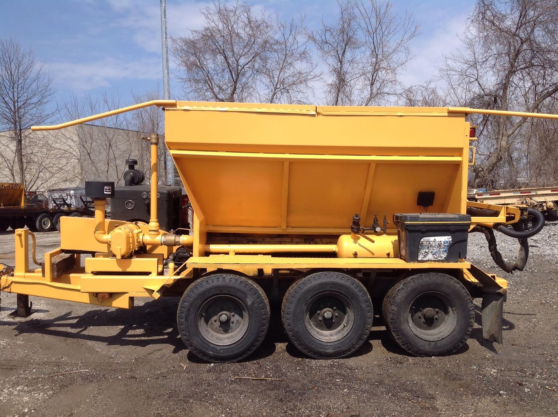 Yellow construction trailer with three wheels, a large hopper, and equipment.