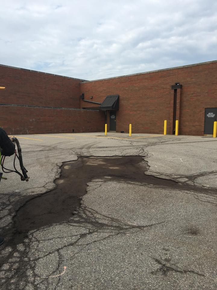 Exterior of a brick building with cracked asphalt. A small black awning covers a door.