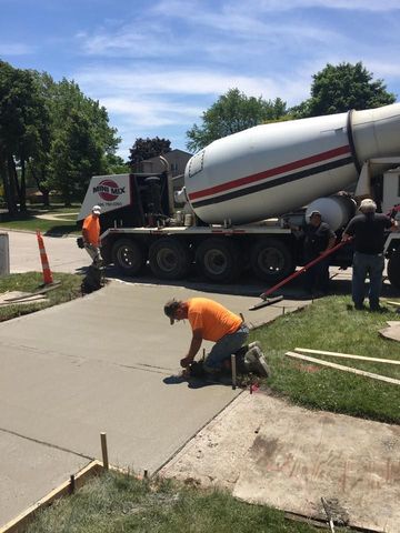 Construction workers pouring and smoothing concrete for a driveway, with a cement truck in the background.