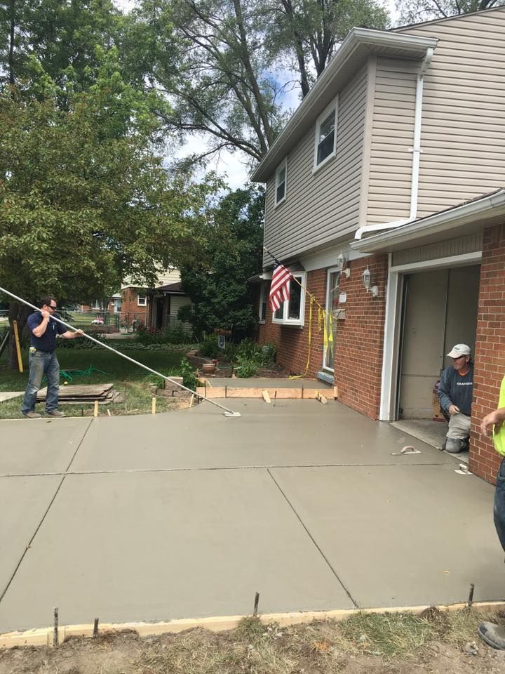 Workers pouring and finishing a new concrete driveway next to a brick house with an open garage door.