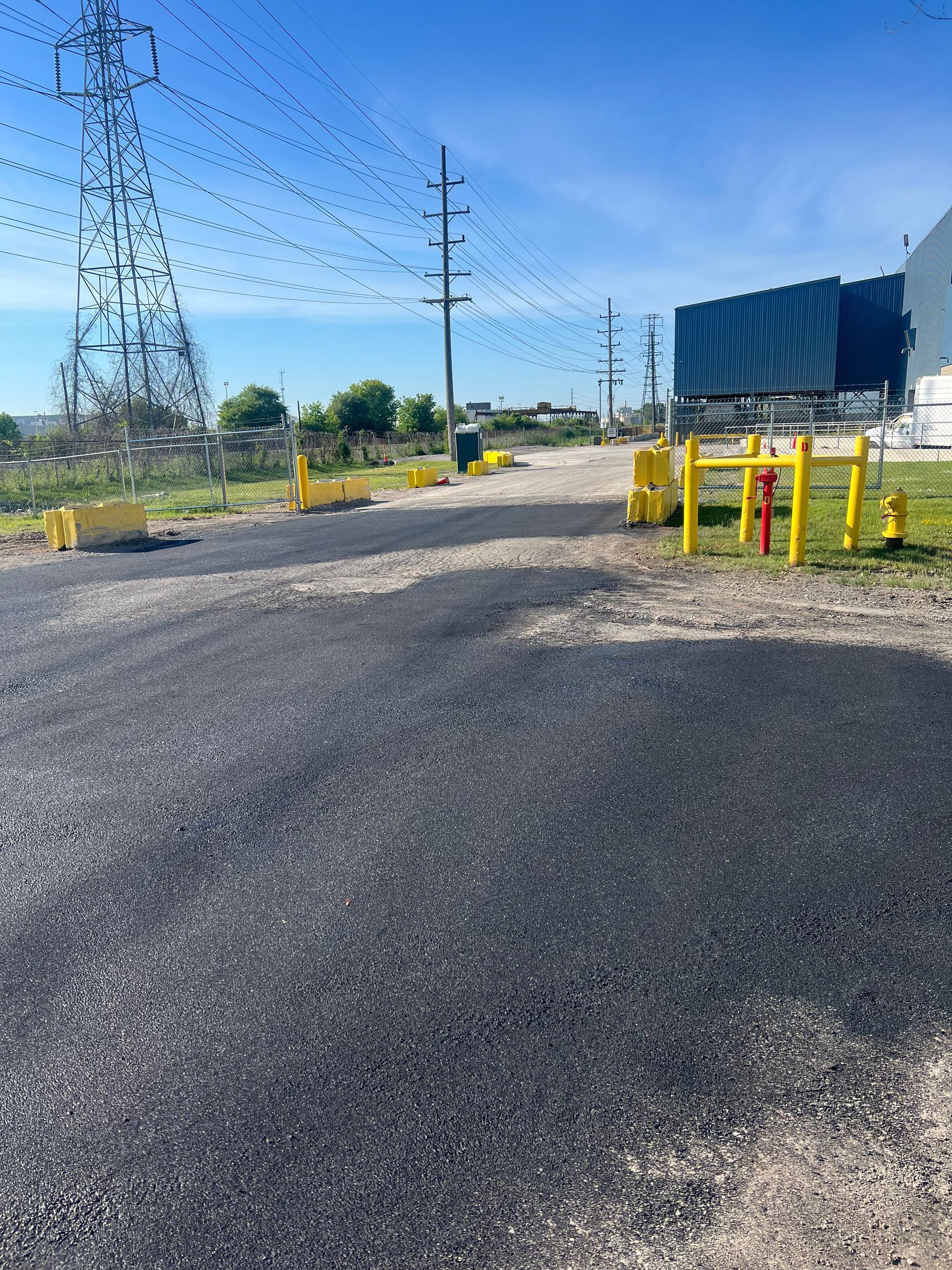 Gravel road beside power lines and yellow barriers under a clear blue sky