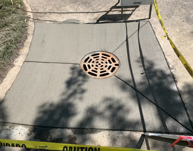 Freshly poured concrete with a drain in a walkway, surrounded by caution tape.