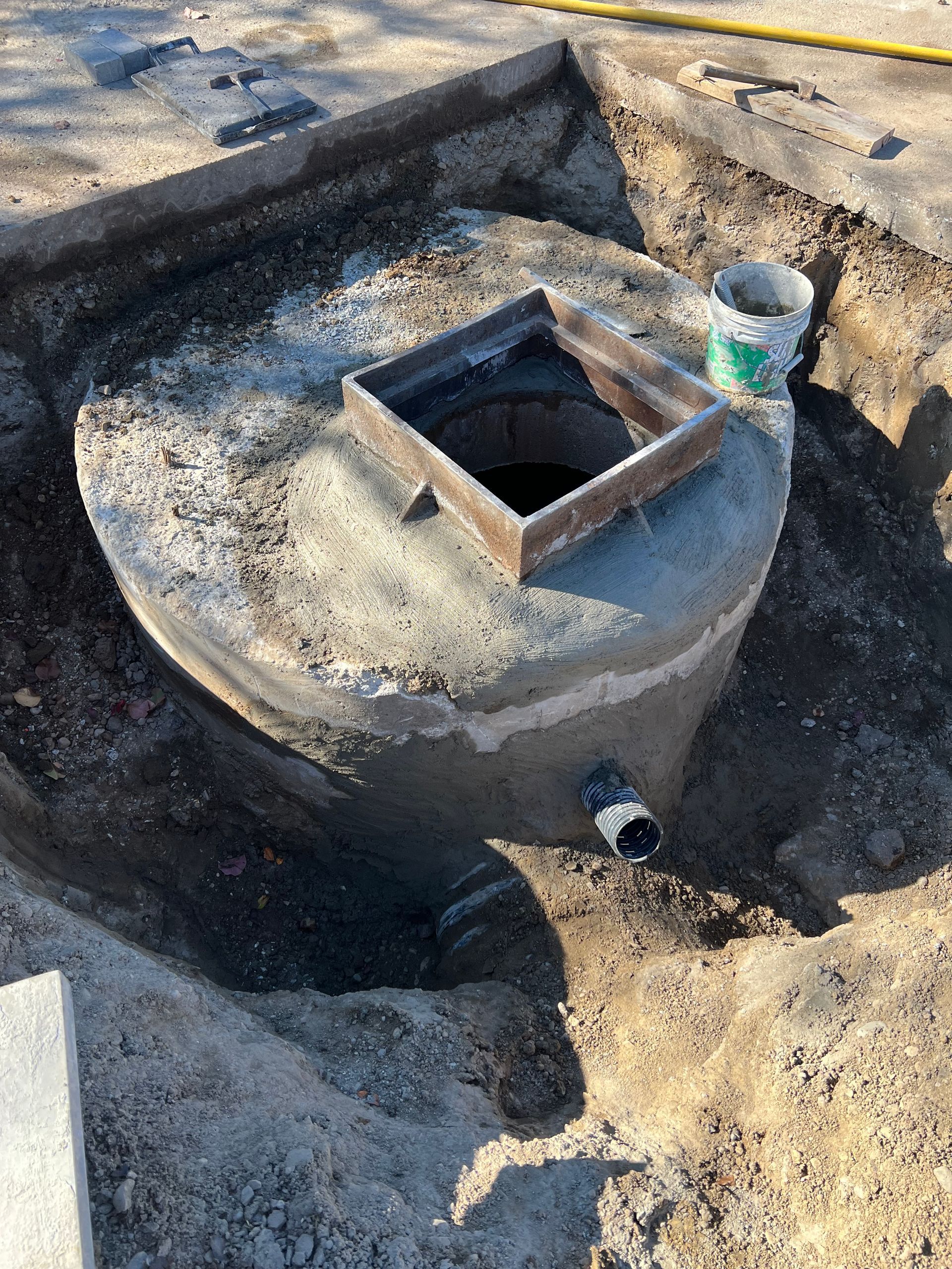 Rooftop concrete vent shaft with square opening and a small pipe, surrounded by weathered tar paper.