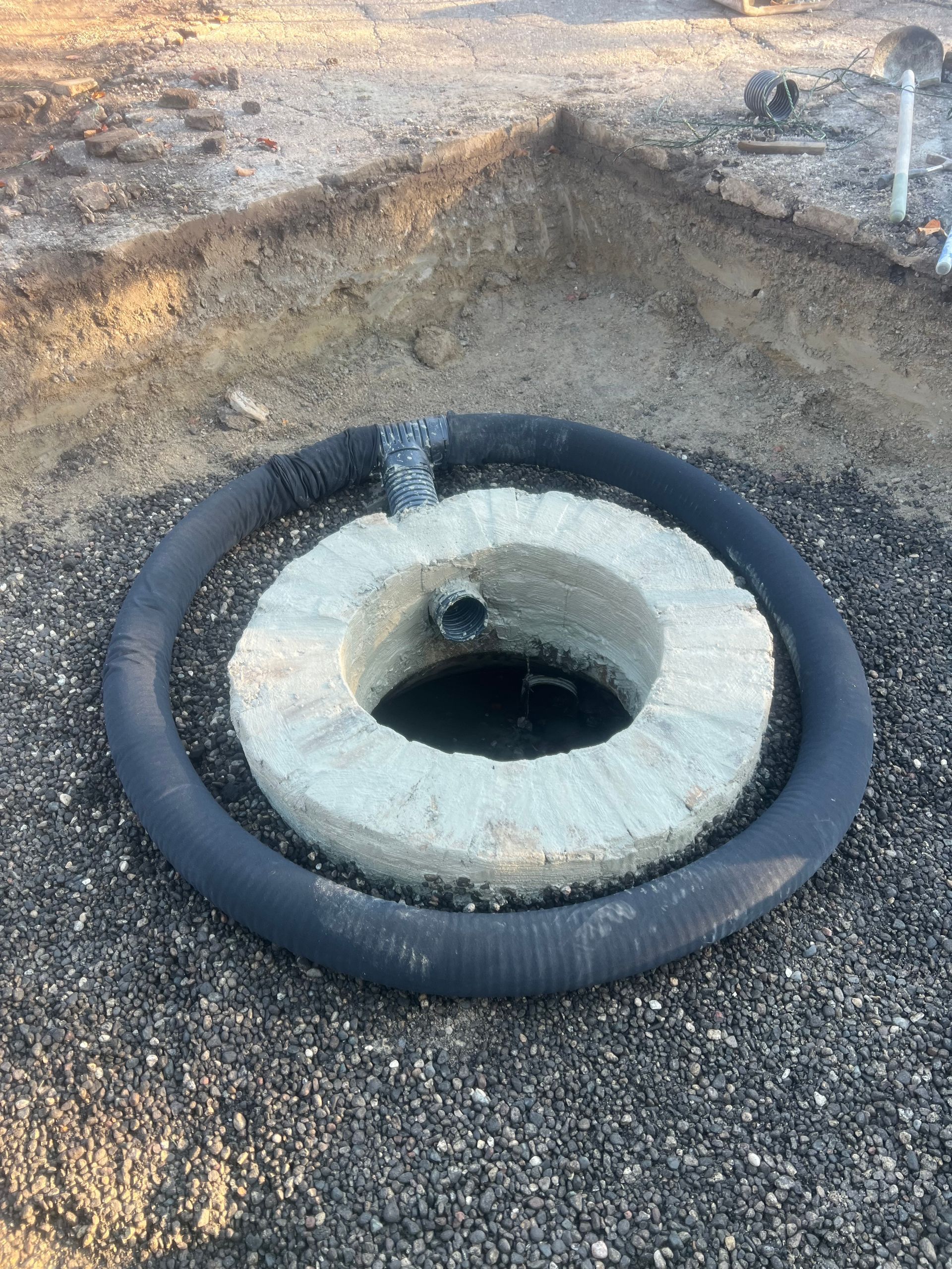 Construction site hole surrounded by a black tire and concrete ring on dirt ground
