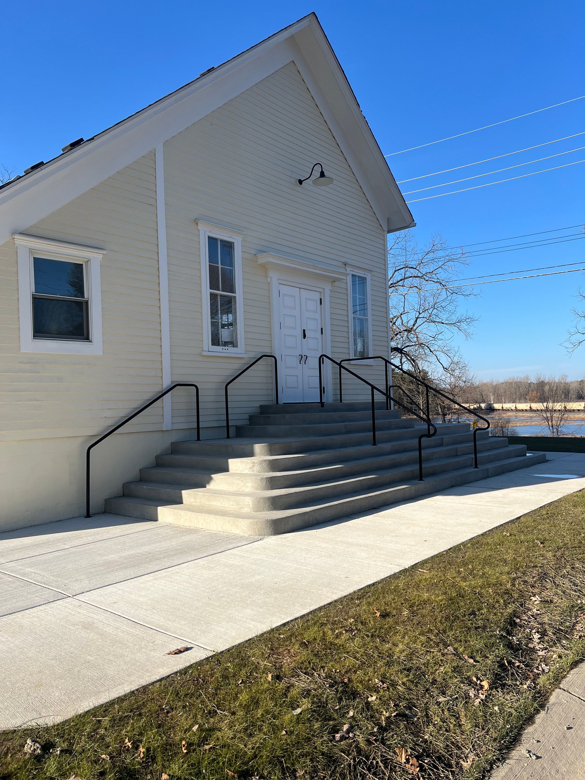 White church entrance with steps, black railings, and a steep gabled roof under a clear blue sky