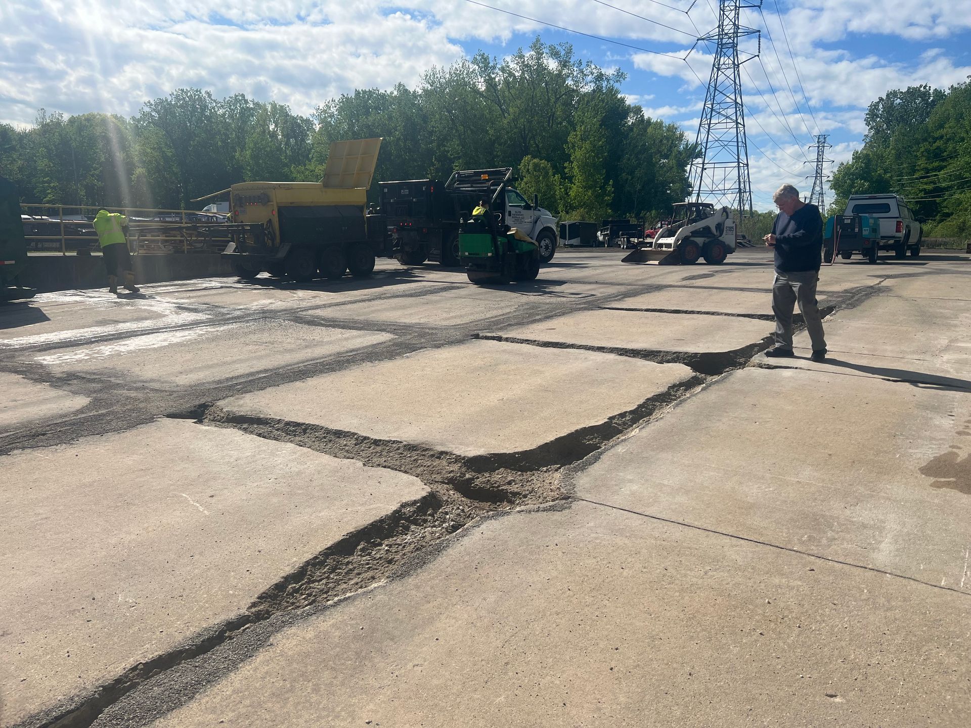 Construction workers repairing cracked concrete pavement with equipment on a sunny site