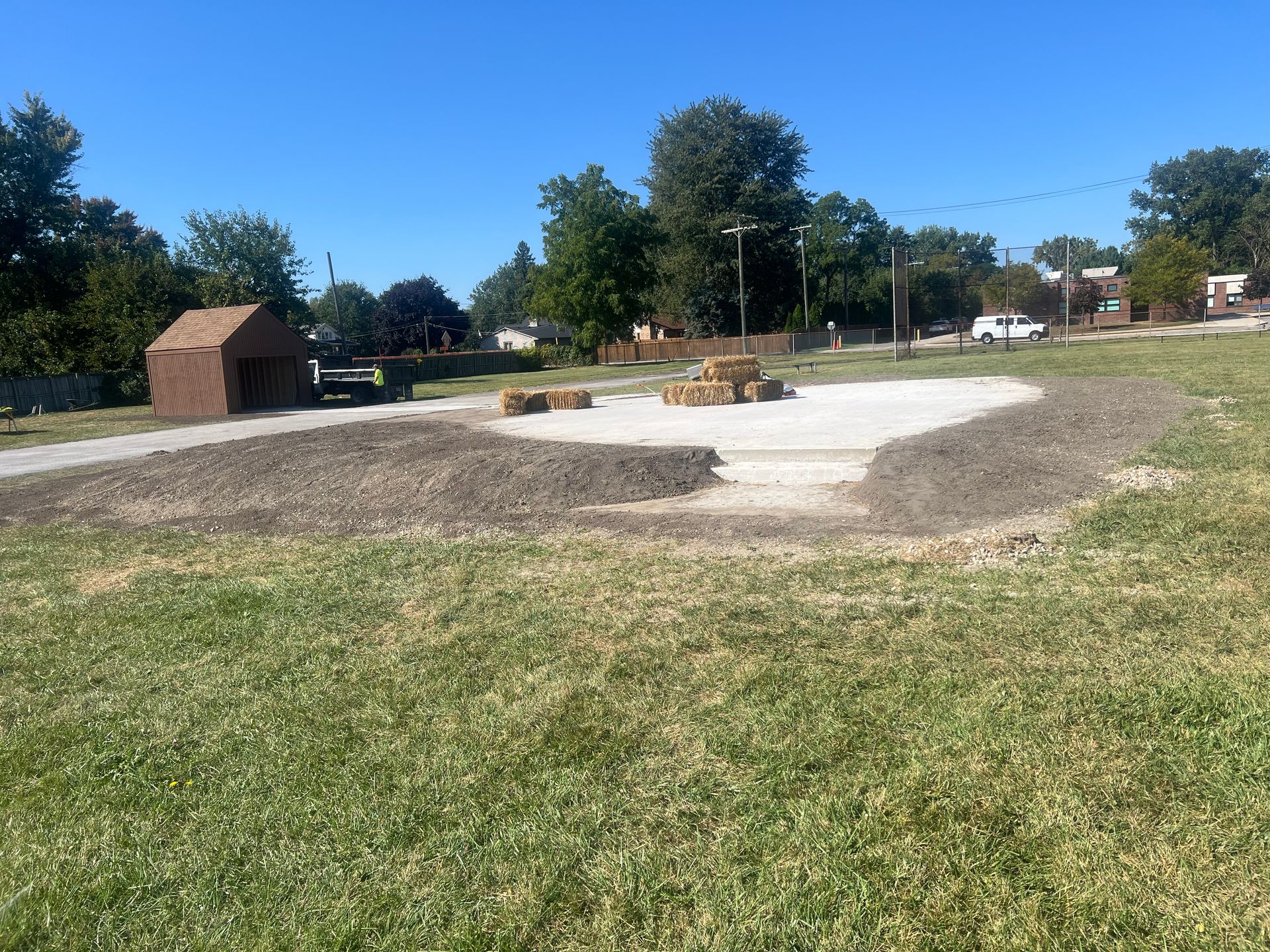 Grassy park with a small brick shelter and a concrete paved area under a clear blue sky