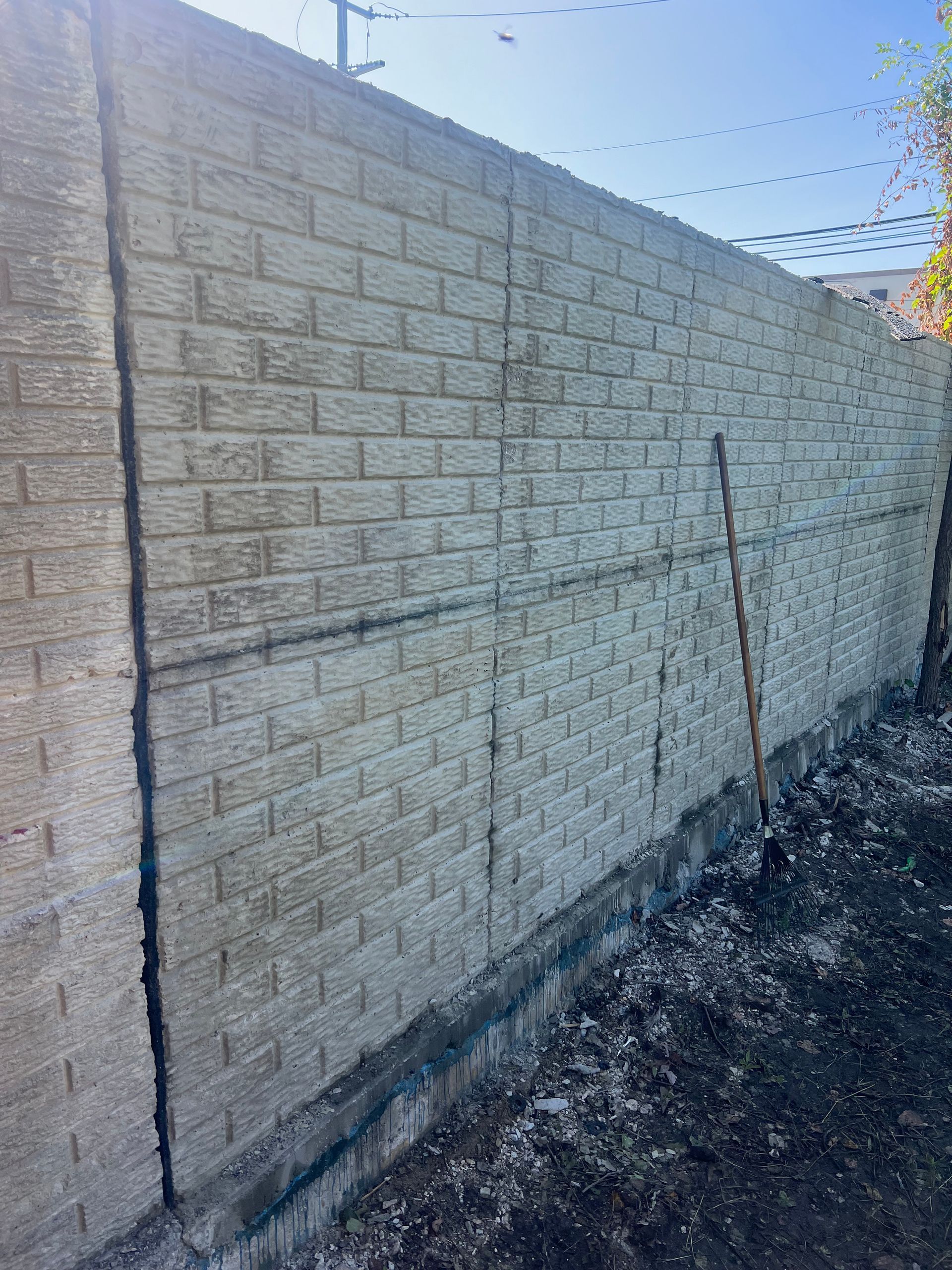 Sunlit beige brick wall with barbed wire along the top beside a dirt path