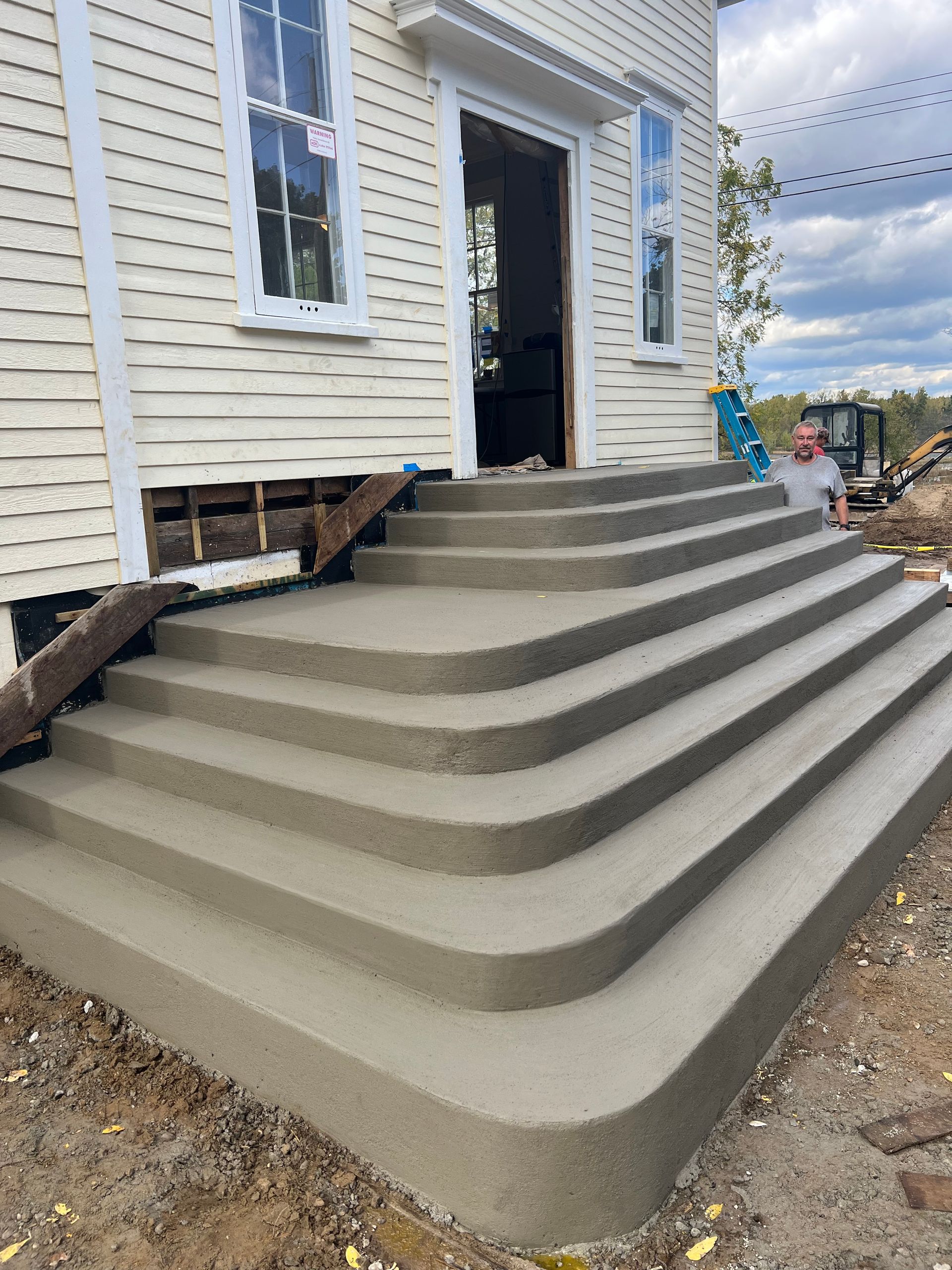 Concrete front steps leading to a house entrance with white siding and a black door.