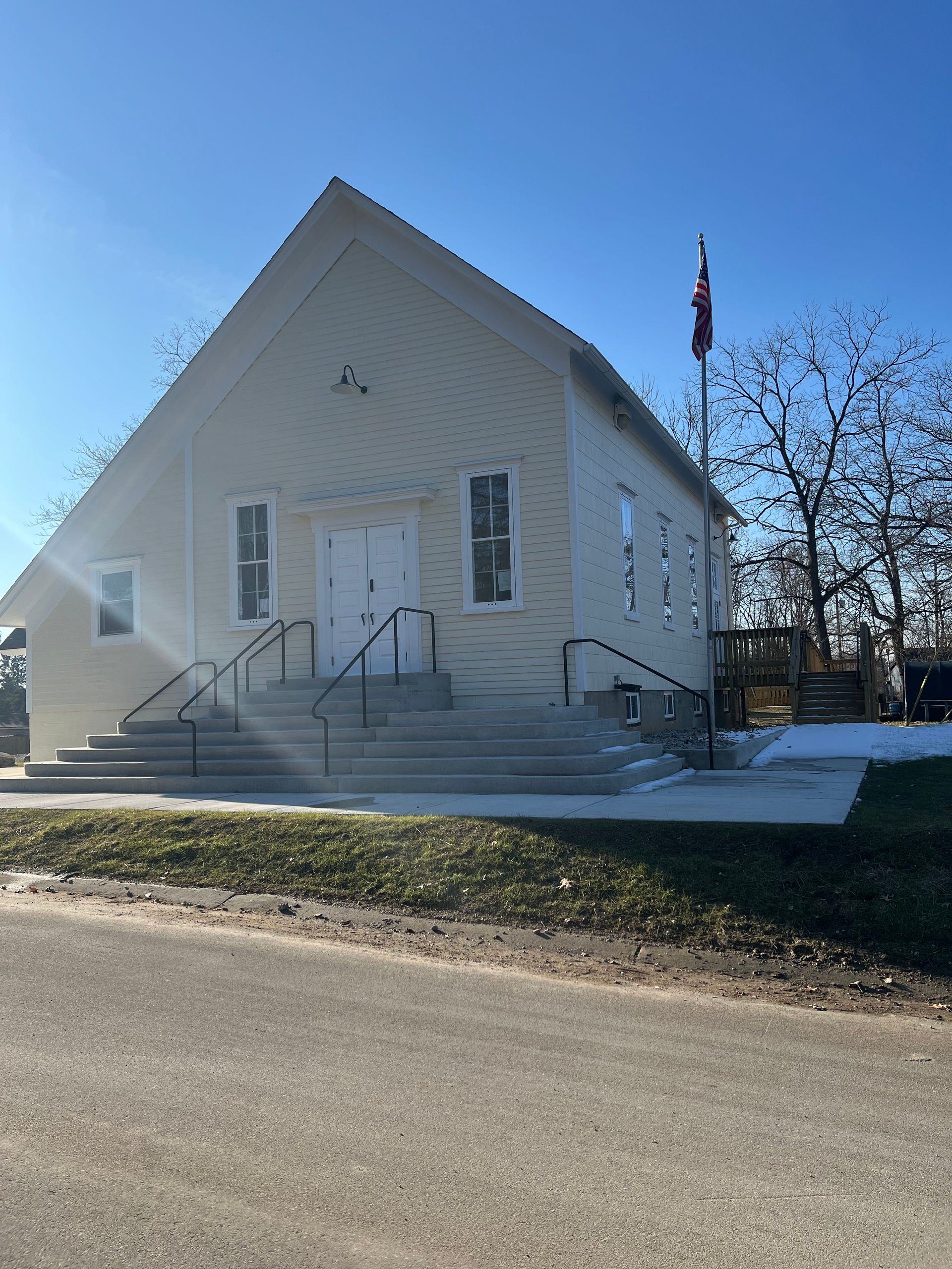 White church with steeple and front steps beside a road on a sunny day