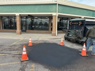 Parking lot with orange cones around a fresh black asphalt patch in front of a store entrance