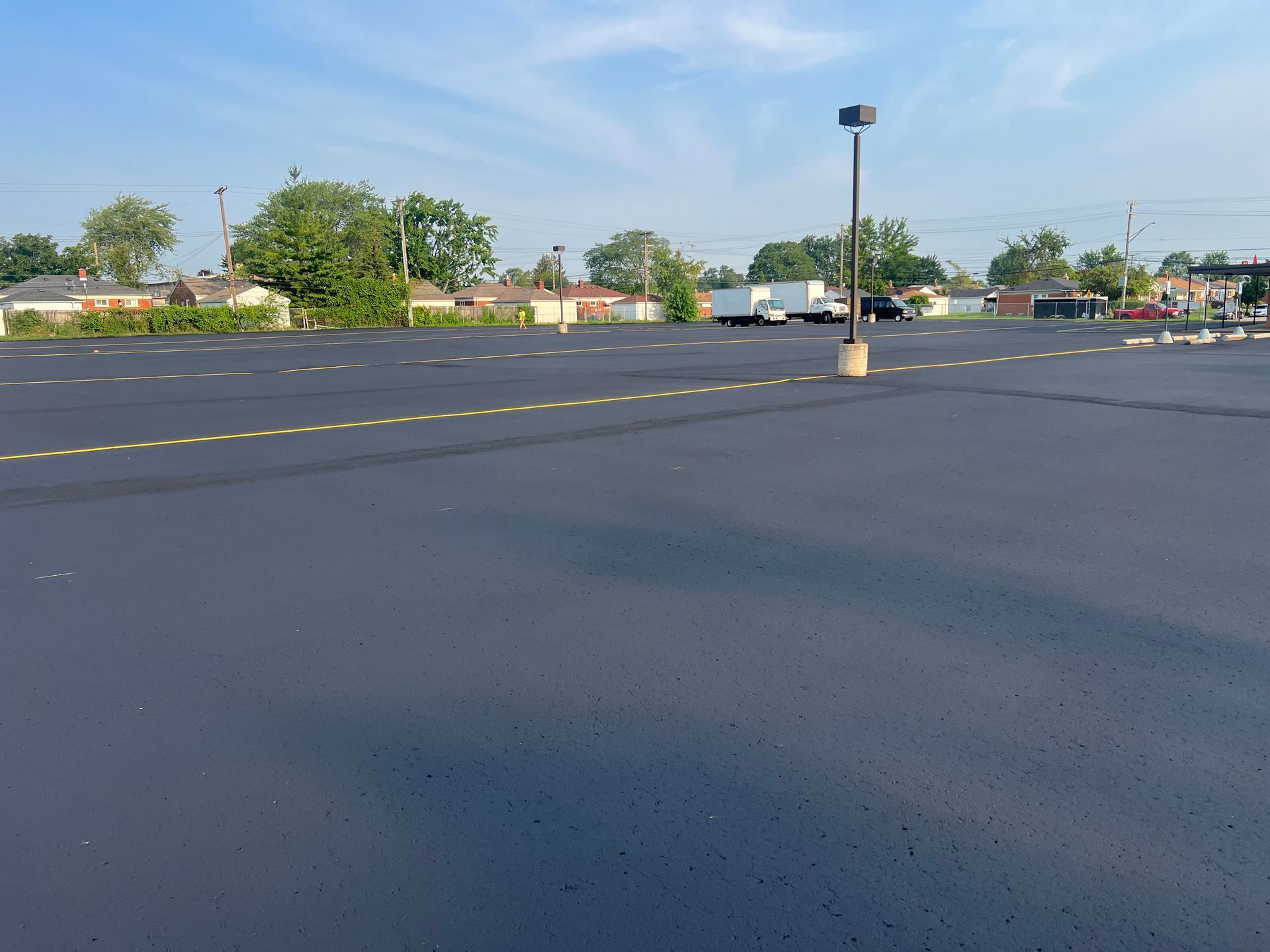 Empty parking lot with yellow lines, a light pole, and trees under a clear blue sky