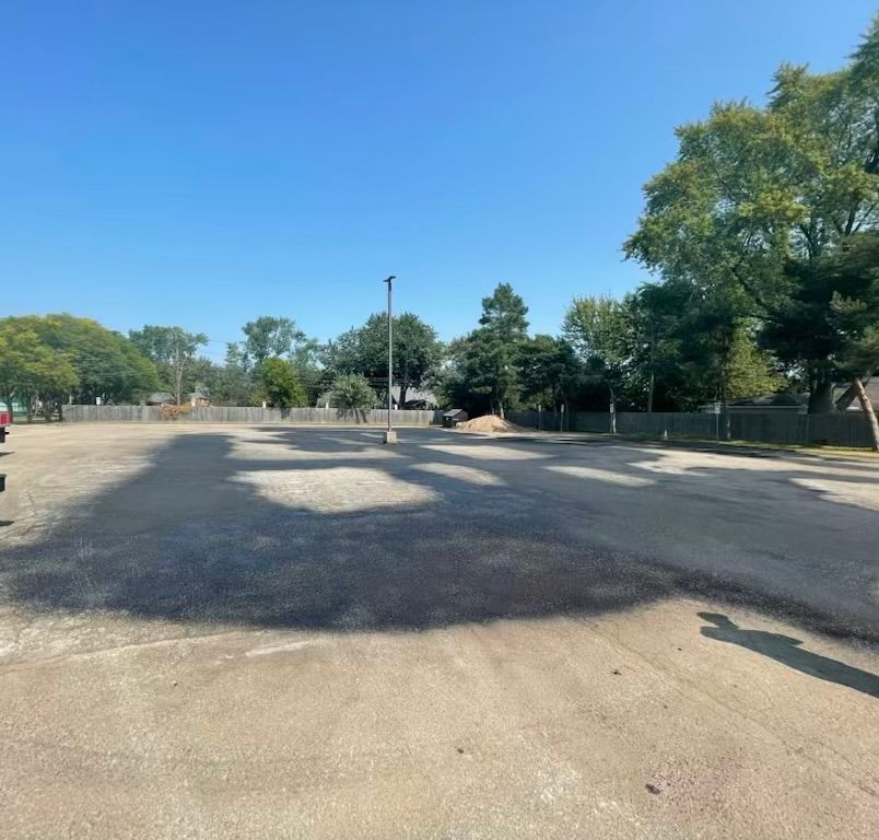 Sunny empty parking lot with trees and a distant utility pole under a clear blue sky