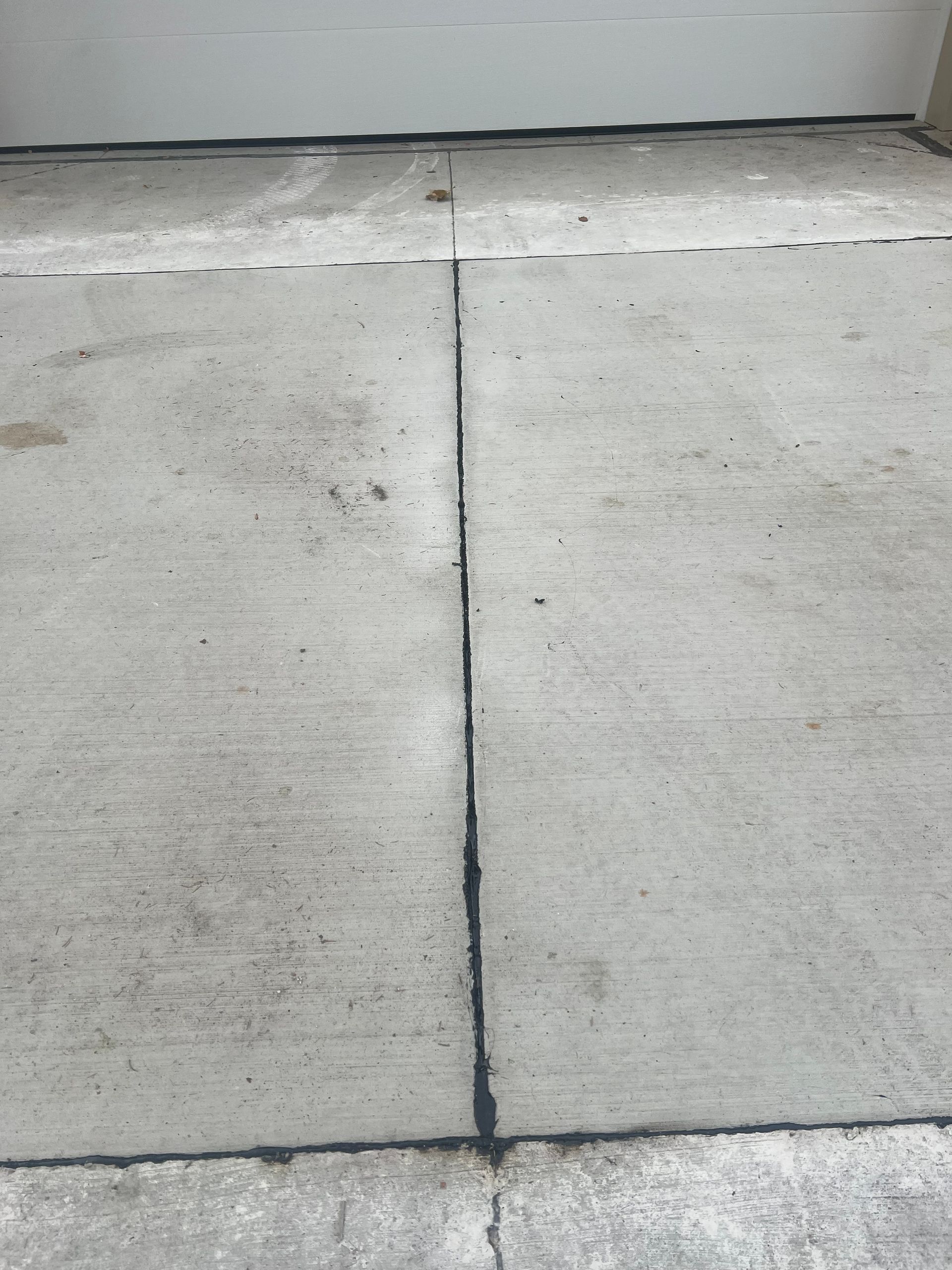 Cracked concrete sidewalk with a dark vertical seam near a curb.