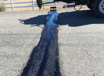 Road repair with dark asphalt in a lane, orange cones, and a white truck parked on the side.