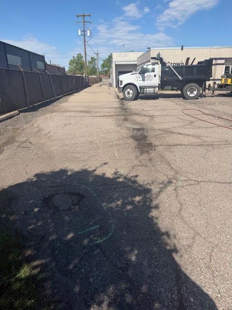 White dump truck on an empty cracked industrial street beside a black fence under a blue sky.