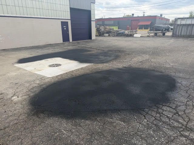 Parking lot with two large black asphalt patches beside an industrial building