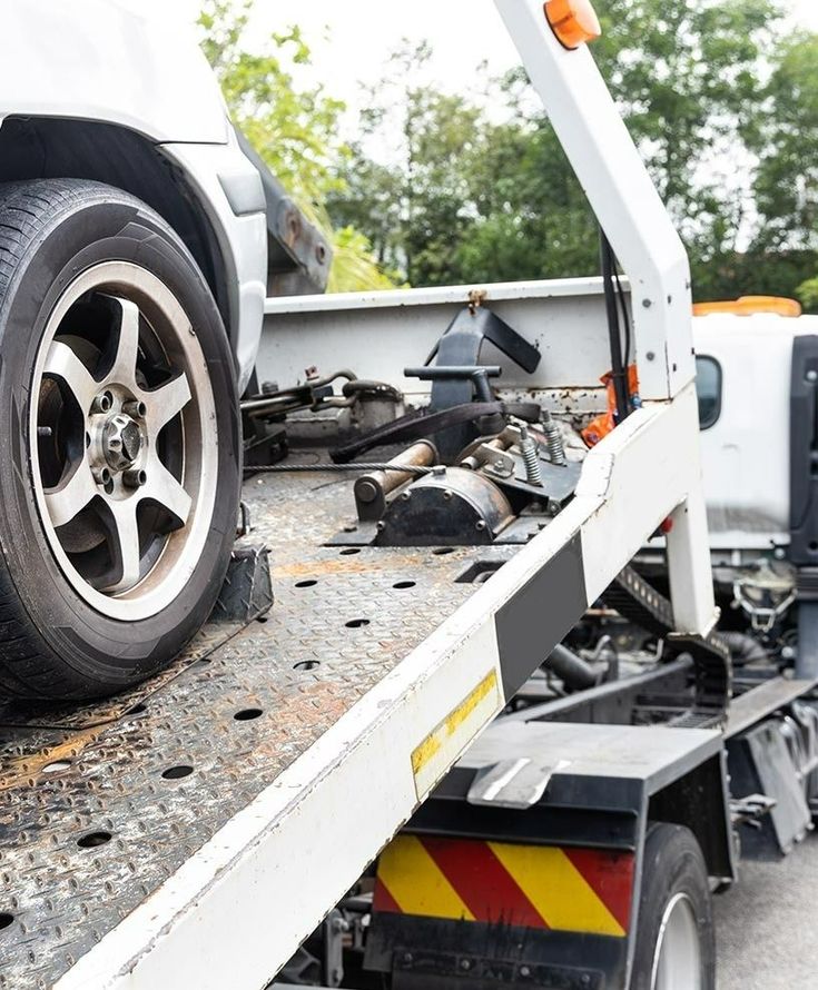 Car loaded on a tow truck flatbed, with wreckage and debris visible on the bed
