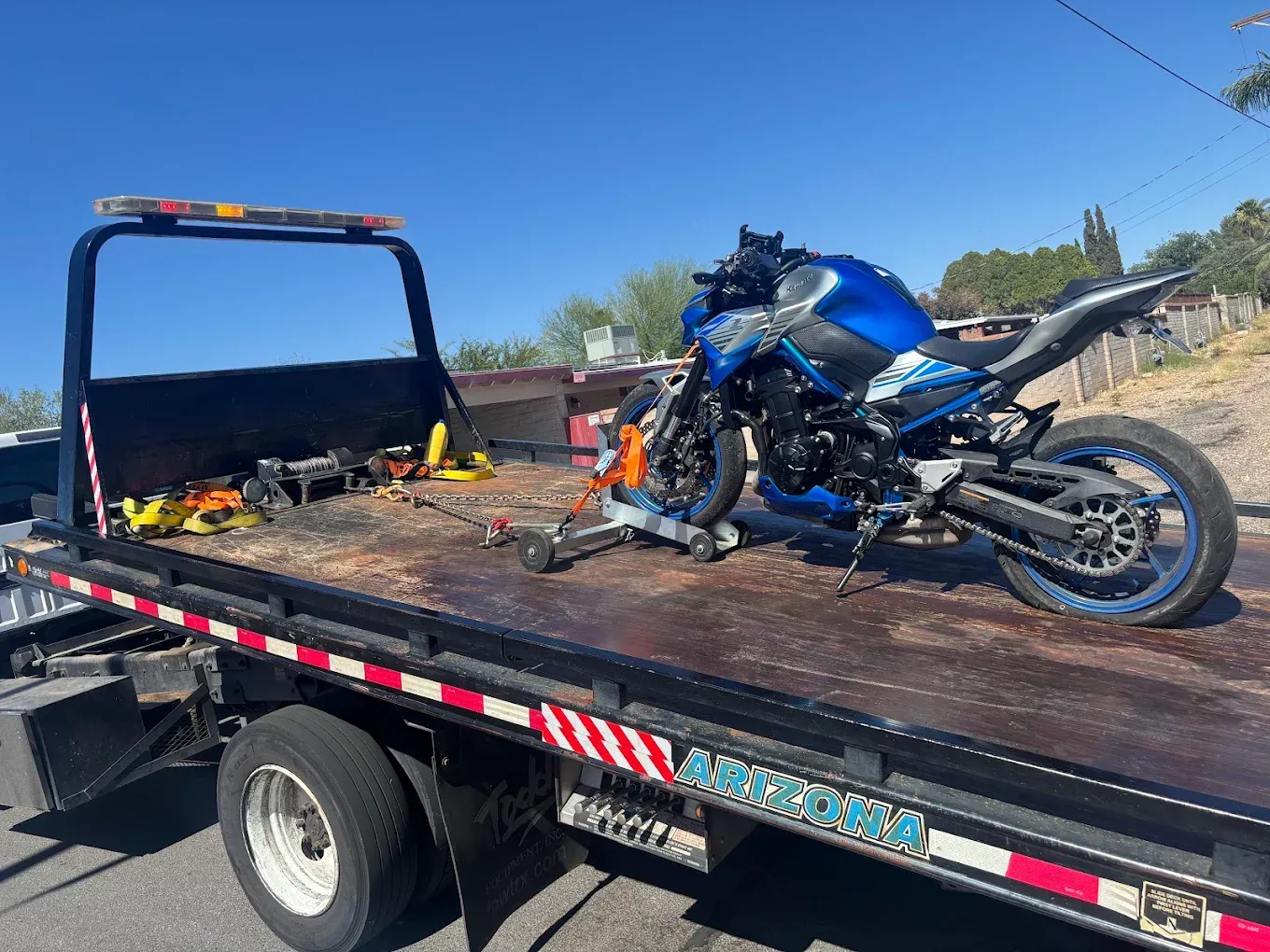 Blue motorcycle wreck on a flatbed tow truck under a clear sky, with debris on the bed.