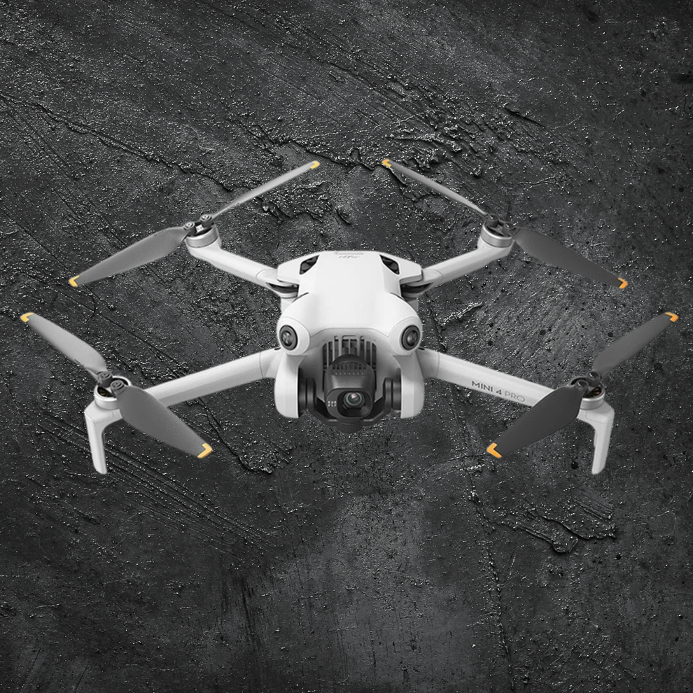 Hand holding a white drone over a beach with blurred ocean in the background